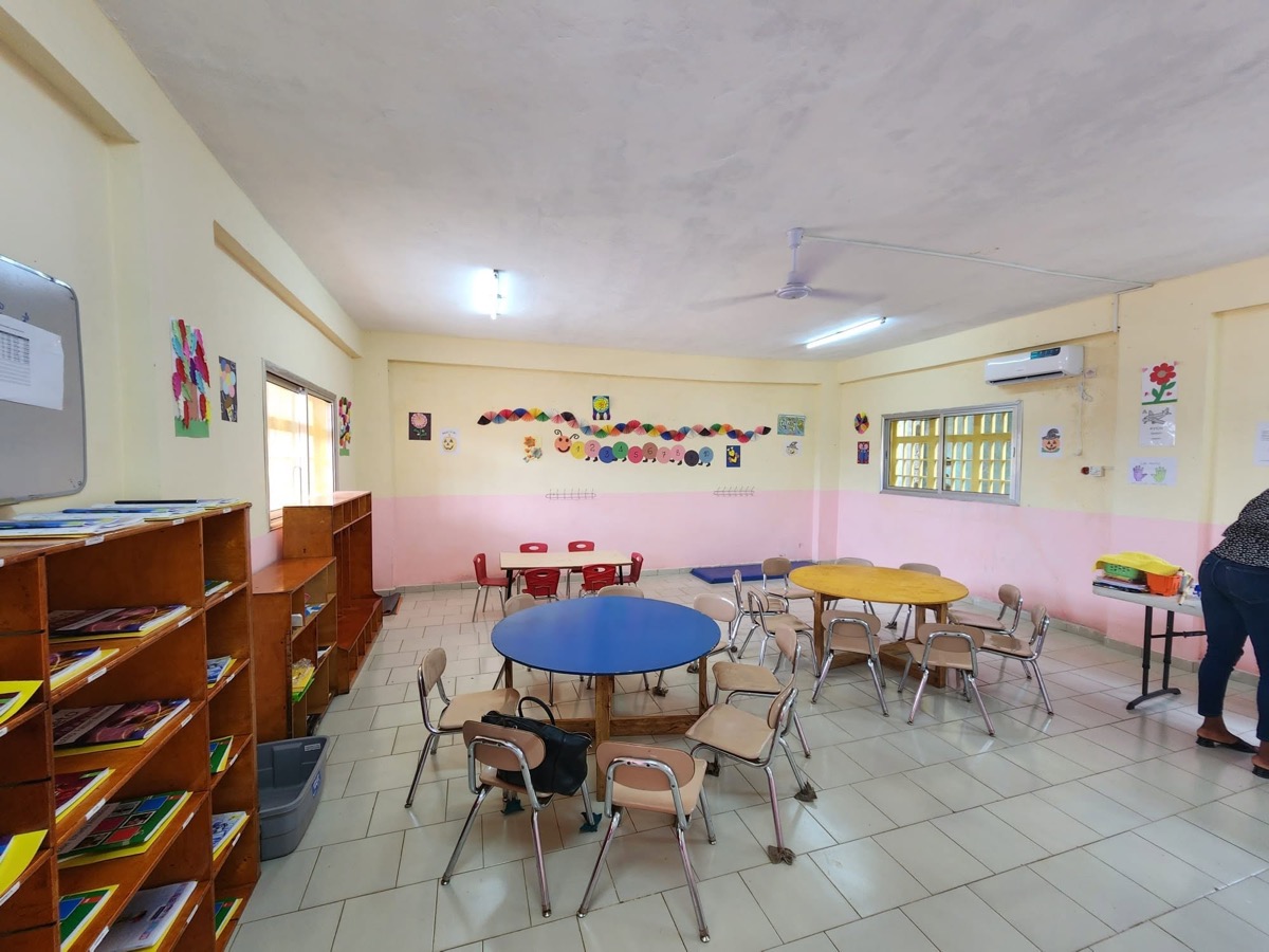 Salle de maternelle aménagée avec tables rondes et coin lecture.
